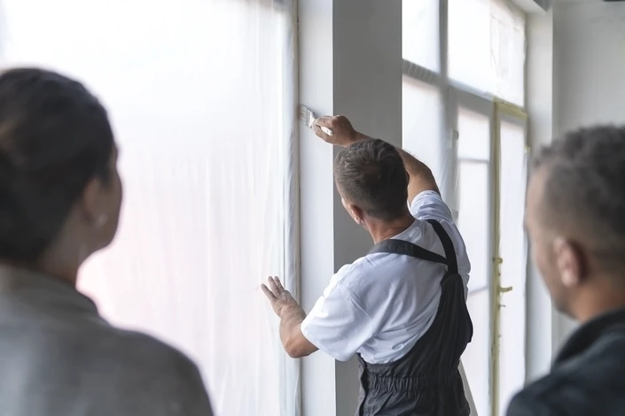 Homme en tenue de travail installant du parquet dans une pièce en rénovation, agenouillé sur le sol, utilisant un marteau pour ajuster les lames de bois
