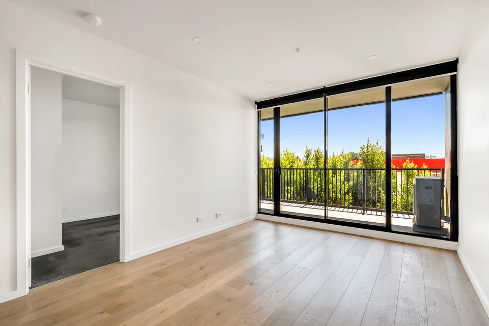 Chambre vide avec parquet stratifié et mur blanc récemment peint dans un appartement rénové avec couloir menant à d'autres chambres