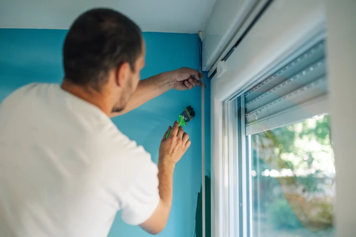 Un travailleur peint avec une brosse autour d'une fenêtre pendant que les clients supervisent le travail