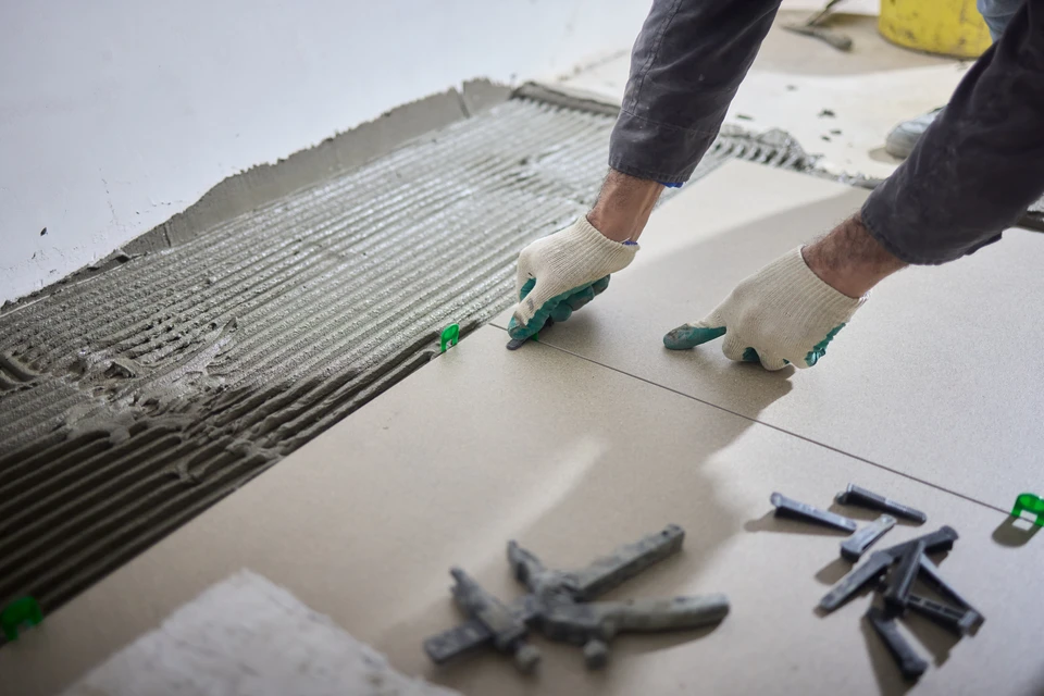 Intérieur en cours de rénovation, artisan carreleur installant du carrelage imitation bois sur chape béton