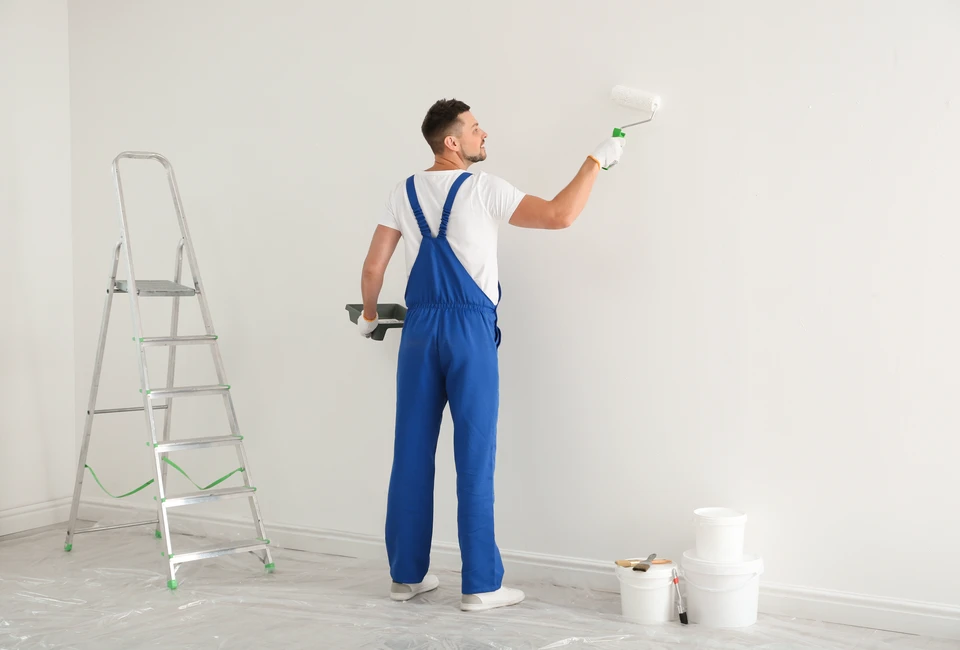 Femme souriante effectuant travaux de peinture murale intérieure, tenant rouleau à peinture avec manchon orange