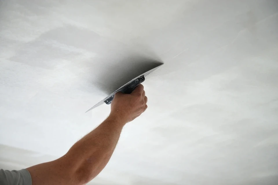 Ouvrier en salopette bleue appliquant de la peinture blanche au plafond d'une pièce en construction avec rouleau à peinture