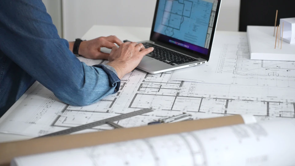 Deux professionnels collaborent sur un projet d'aménagement intérieur, consultant plans architecturaux et nuanciers de couleurs autour d'une table en bois