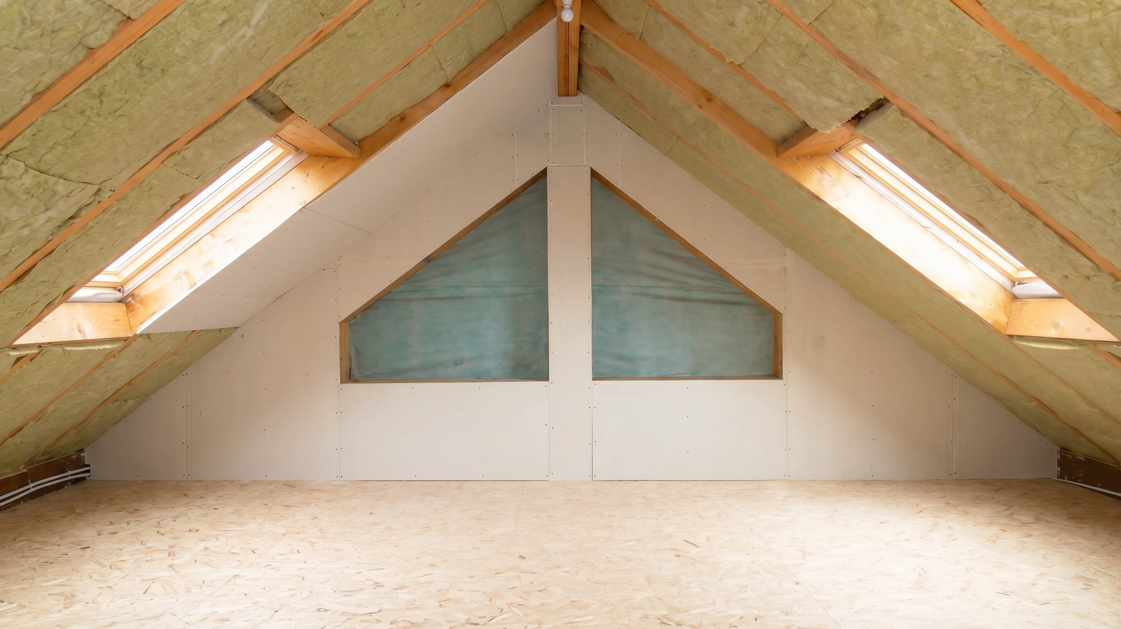 Ouvrier en combinaison blanche et masque respiratoire installant des panneaux d'isolation thermique dans les combles d'une habitation